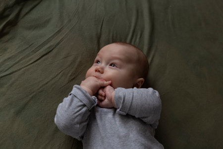 An adorable baby gazes curiously, hands near face, embodying innocence and calmの写真素材