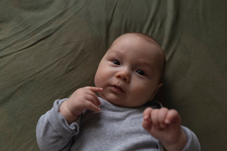 An adorable baby gazes curiously, hands near face, embodying innocence and calmの写真素材