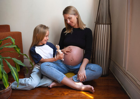A pregnant mother and her daughter share a joyful moment at home, full of loveの写真素材