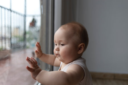 A curious baby exploring the world through a window, full of wonder and innocenceの写真素材