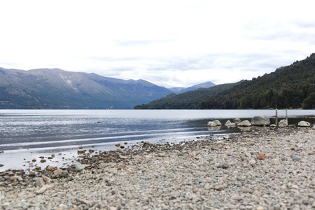 A tranquil lakeshore with mountains in the background under a cloudy skyの写真素材
