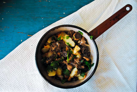 Fried potatoes with mushrooms, onions and parsley in a frying pan on a turquoise wooden tableの写真素材