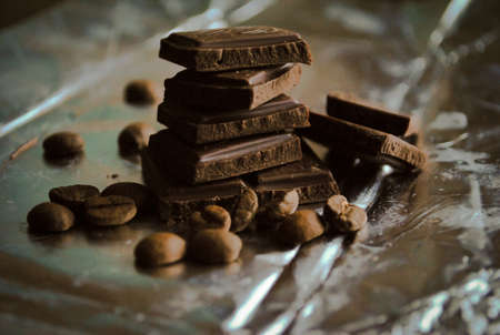 Stack of milk chocolate slices and brown coffee beans on a foilの写真素材