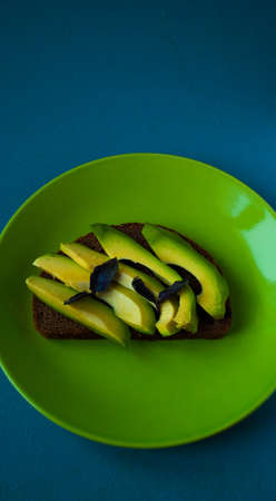 Sandwich with avocado slices on rye bread lies on green plate