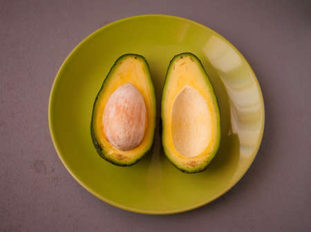 Top view of halved avocado lie on light green plate