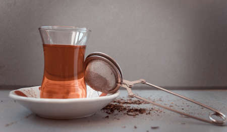 Turkish tea in traditional glass and tea strainer in a pile of tea leaves on a light gray background. Toned imageの写真素材
