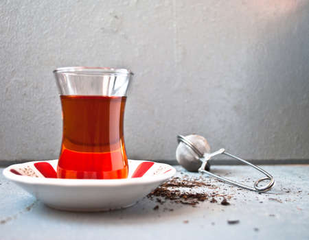 Turkish tea in traditional glass and tea strainer in a pile of tea leaves on a light gray backgroundの写真素材