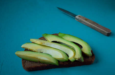 Avocado sandwich with rye bread and knife lies on the turquoise backgroundの写真素材