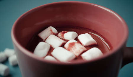 Pink cup of hot cocoa with marshmallows on turquoise background. Close up
