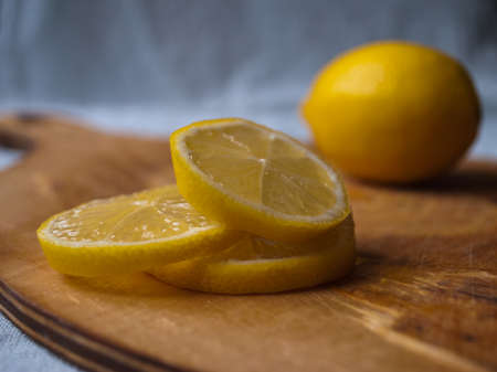 Stack of bright yellow lemon slices and whole lemon on brown rustic wooden cutting boardの写真素材