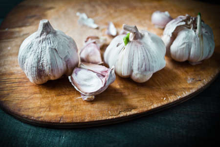 Fresh raw garlic on beige cutting board and dark turquoise wooden table. Close upの写真素材
