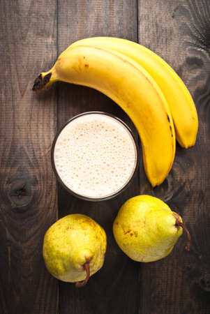 Glass of smoothie and fresh bananas and pears on wooden background.の写真素材