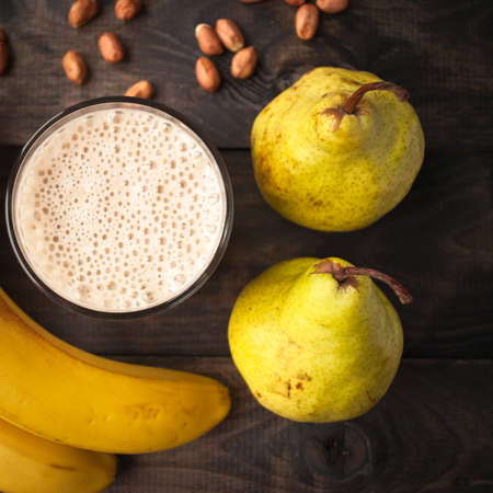 Glass of smoothie, some peanuts, fresh bananas and pears on wooden backgroundの写真素材