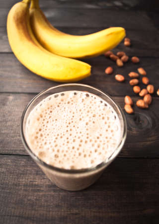 Smoothie with bananas and some peanuts on brown rustic wooden backgroundの写真素材