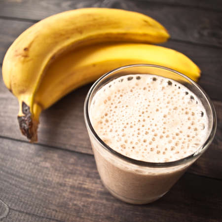 Glass of banana smoothie and fresh bananas on brown wooden backgroundの写真素材