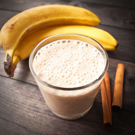 Smoothie, cinnamon sticks and fresh bananas  on wooden backgroundの写真素材