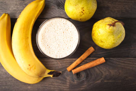Glass of smoothie, cinnamon sticks, fresh bananas and pears on wooden background. Top viewの写真素材