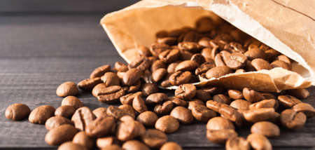 Coffee beans in beige paper bag on wooden backgroundの写真素材