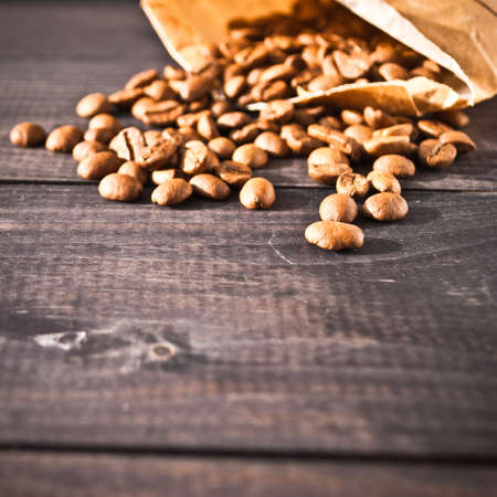 Coffee beans in beige paper bag on rustic wooden backgroundの写真素材