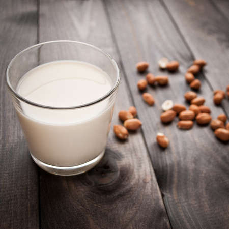 Glass of milk and some peanuts on brown wooden backgroundの写真素材