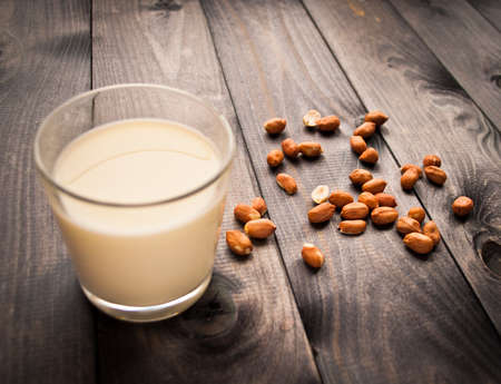 Glass of milk and some peanuts on wooden surfaceの写真素材