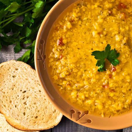Red lentil soup in brown bowl, parsley and toast of white bread on wooden background.Top viewの写真素材
