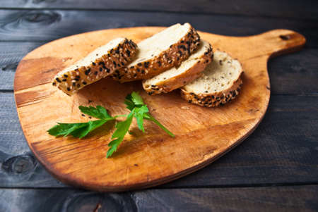 Slices of fresh baguette with sesame and parsley on wooden cutting boardの写真素材