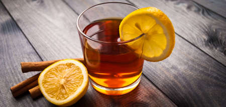 Cup of black tea, cinnamon sticks, lemon slice on the edge of the cup and half of lemonの写真素材