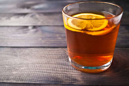 Lemon slice in a cup of black tea on wooden background