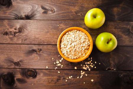 Rolled oats in bowl and two green apples on rustic wooden surface. Copy space