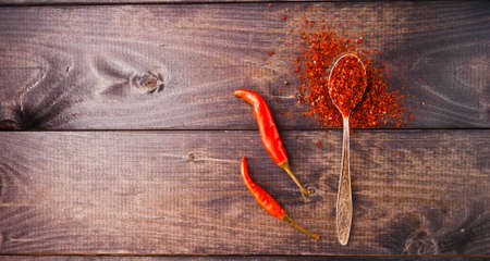 Full spoon of ground chili pepper and two whole fresh red chiliesの写真素材