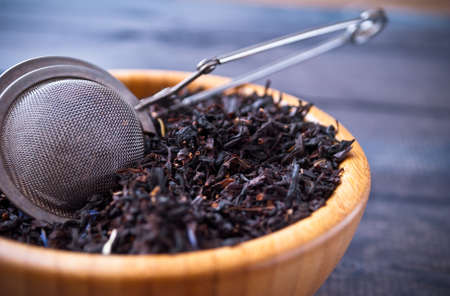 Dried tea leaves in bamboo bowl and tea strainer on wooden background. Close upの写真素材