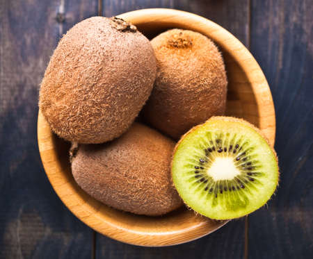 Three whole and one half of kiwi fruit in a bowl on rustic wooden backgroundの写真素材