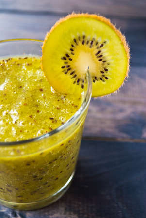 Fresh green smoothie from kiwi fruit and one slice of fruit on the edge of glass on wooden backgroundの写真素材