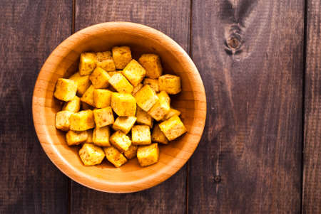 Bowl of fried tofu cubes with curry on shabby wooden backgroundの写真素材
