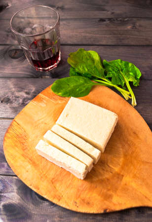 Slices of raw tofu on shabby cutting board, green leaves of fresh spinach and glass of red wine on rustic wooden backgroundの写真素材
