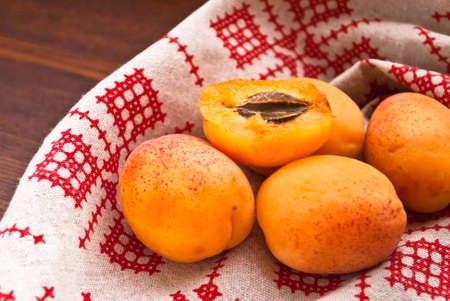 Raw apricots on a napkin with red pattern and on a wooden background. Close up
