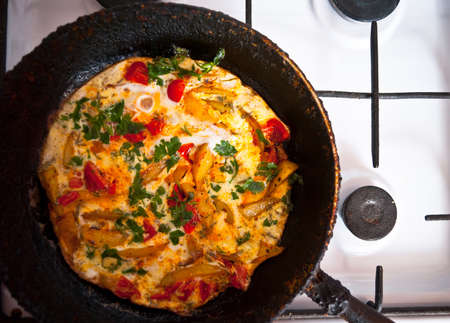 Homemade fritatta with tomatoes, parsley and fried potato in the old cast iron frying pan and on the...