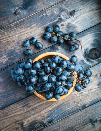 Bunch of black grapes in a bamboo bowl on a shabby wooden backgroundの写真素材