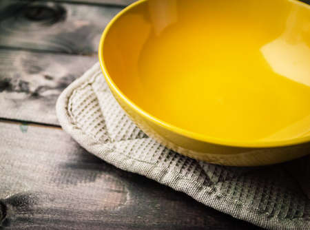 Empty yellow soup plate lies on a gray cotton potholderの写真素材