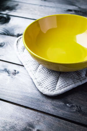 Empty yellow soup plate lies on a gray potholder with wooden backgroundの写真素材