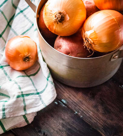 Raw potatoes and onions. Ingredients for cooking in a pan with kitchen towel besideの写真素材