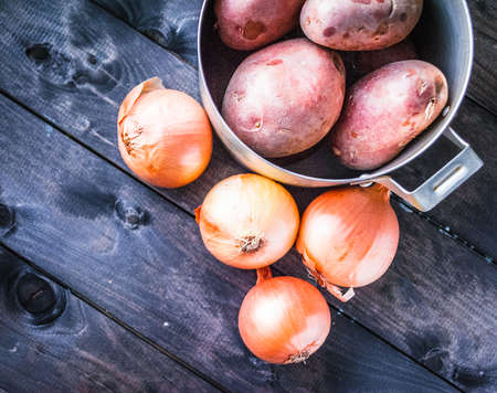 Raw potatoes in a pan and onions beside, top viewの写真素材