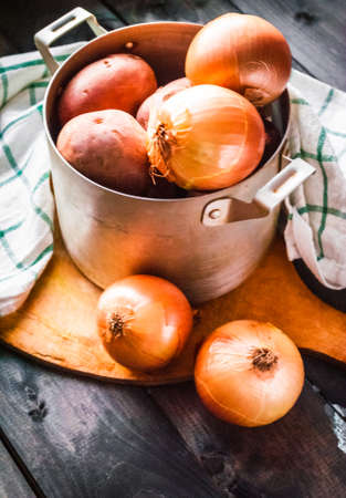 Raw potatoes and onions. Ingredients for cooking in a pan on a cutting board with kitchen towel besideの写真素材