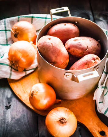 Raw potatoes in a pan and onions on a cutting board with kitchen towel beside, top viewの写真素材