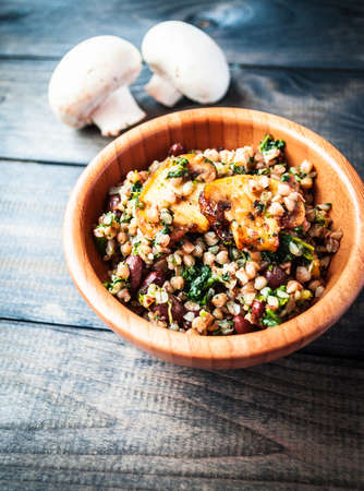 Bamboo bowl of boiled buckwheat, spinach and red beans with slices of fried champignon on the top and couple of raw uncooked whole mushrooms on the backgroundの写真素材