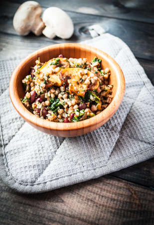 Bamboo bowl of tasty vegan meal on a grey potholder and two raw uncooked mushrooms on the background. Banner or menu pageの写真素材
