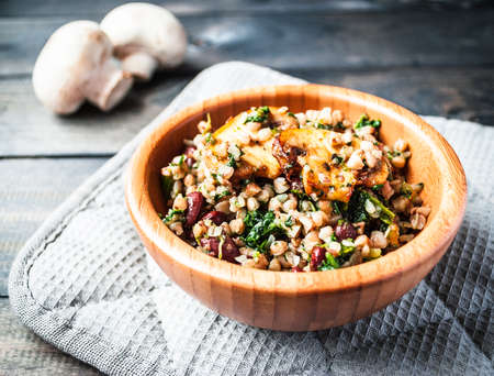 Bamboo bowl of tasty vegan meal on a grey potholder and two raw uncooked mushrooms on the background. Close upの写真素材
