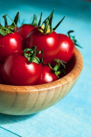 Ripe red cherry tomatoes in a bowl on a turquoise wooden backgroundの写真素材