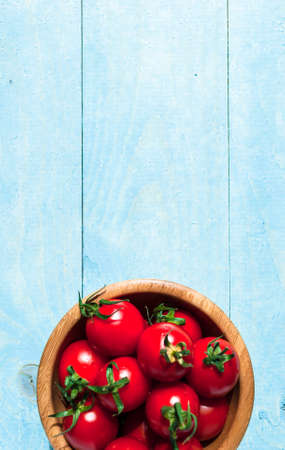 Ripe red cherry tomatoes in a bowl on a turquoise wooden table. Top view. Space for textの写真素材